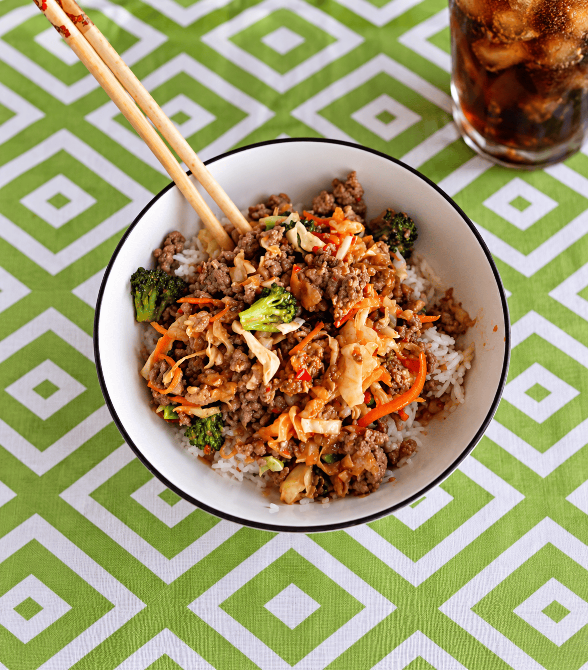 A bowl of rice, ground pork, and vegetables with chopsticks in the bowl.
